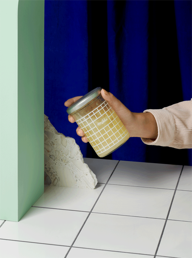 still-life advertising photography gif of had shaking yellow sauce in a glass jar kobalt blue wall
